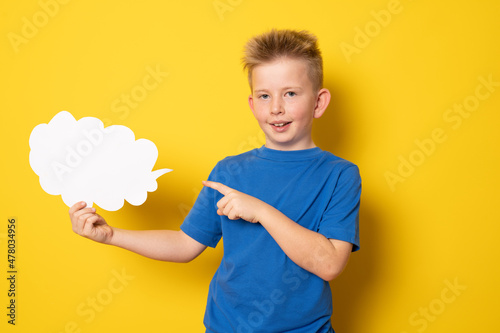 Cute child boy in blue t-shirt showing paper cloud standing isolated over yellow background.