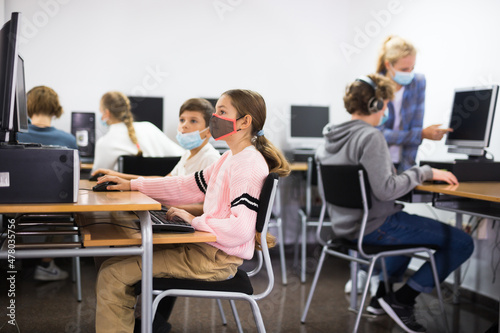 Group of young girls and boys in face masks sitting in computer classroom and exercising.
