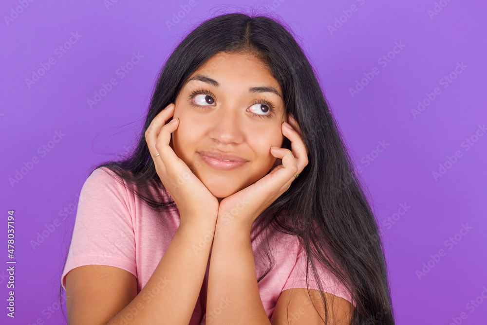 Inspired Hispanic brunette girl wearing pink t-shirt over purple background looking at copyspace having thoughts about future events Inspired Hispanic brunette girl wearing pink t-shirt over purple background looking at copyspace having thoughts about future events