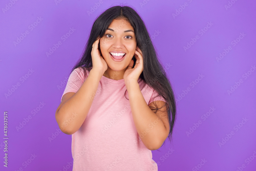Hispanic brunette girl wearing pink t-shirt over purple background Pleasant looking cheerful, Happy reaction Hispanic brunette girl wearing pink t-shirt over purple background Pleasant looking cheerful, Happy reaction