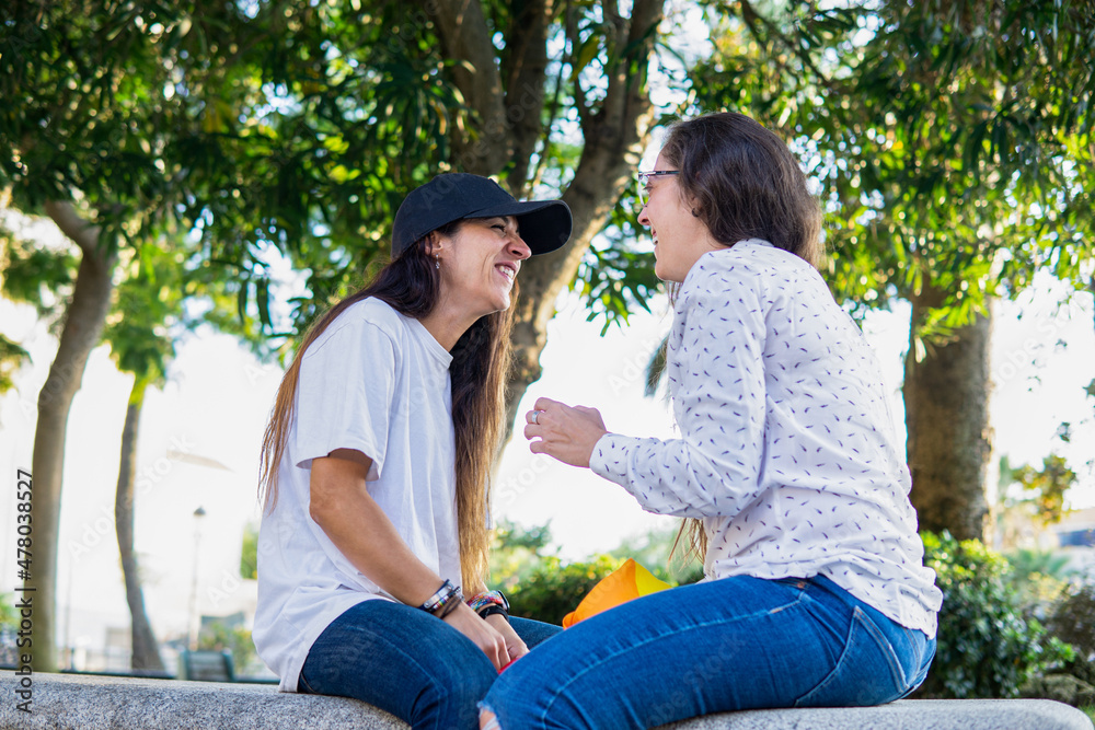 Couple of lesbian girls sitting in park joking around and smiling Couple of lesbian girls sitting in park joking around and smiling