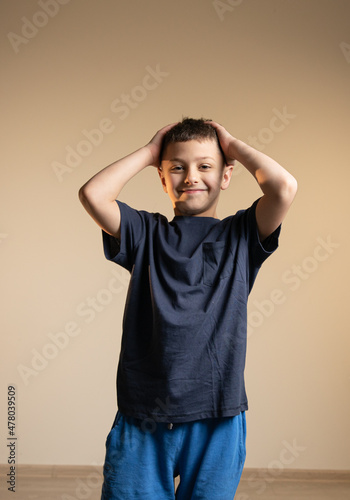 boy in blue t-shirt holds his head with his hands with a happy and self-sufficient expression on his face