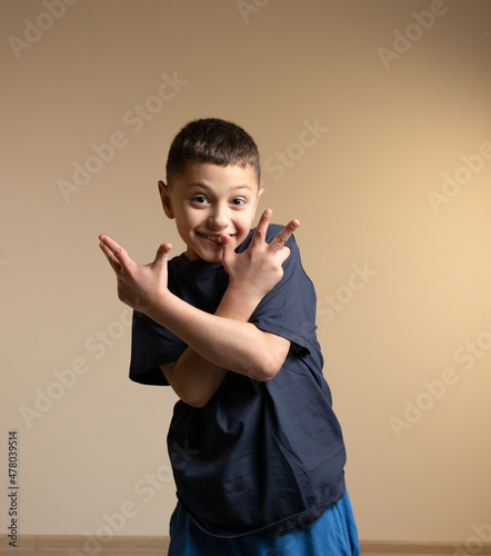 a boy in a blue t-shirt expresses happy emotions, crossed his arms in front of him and with his fingers shows victory