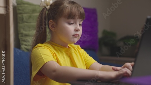 a child girl does her homework on a laptop, online distance learning on computer, schoolgirl does her homework, little kid wants to get a school education, play game on Internet, chat with classmates © Валерий Зотьев