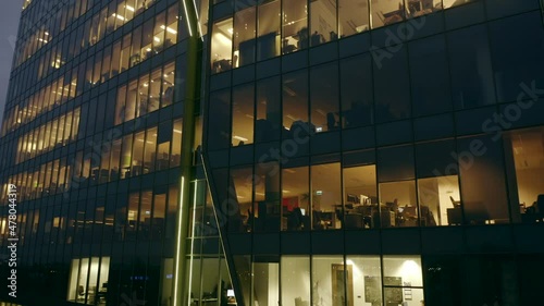 Drone shot up at the windows of a night skyscraper. Opening hours in the office building at night. The drone's flight from the bottom up to the length of an office skyscraper
