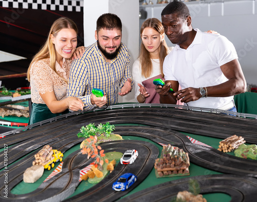 Friendly team of young people is playing with slot car model racing track indoor