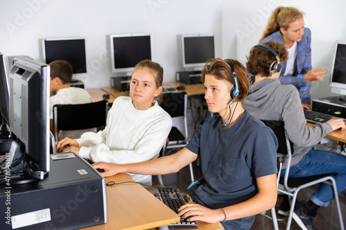 Teenager girls and boys studying in computer lab during lesson.