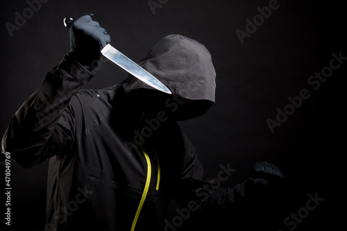 Unknown, indistinguishable maniac or maniac in black with knife attacks the victim with a knife. Concept: Crime because of crisis. Isolated on black background. Selective focus