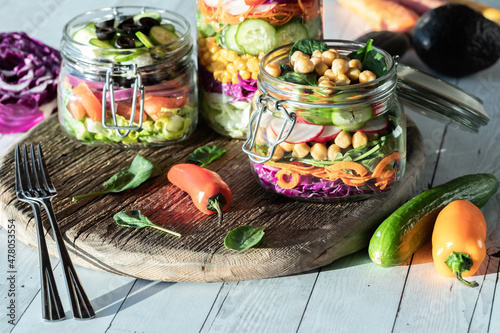 Salad jars on a rustic wooden board with bright sunlight streaming in.