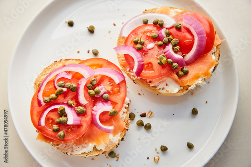 Top View of Lox, Tomatoes, Capers, Red Onion, and Cream Cheese on Bagel on White Plate