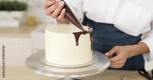 White cake garnished by pastry-cook with chocolate. Rotating. Close-up of hands. The concept of cooking cakes and desserts. Home confectionery.