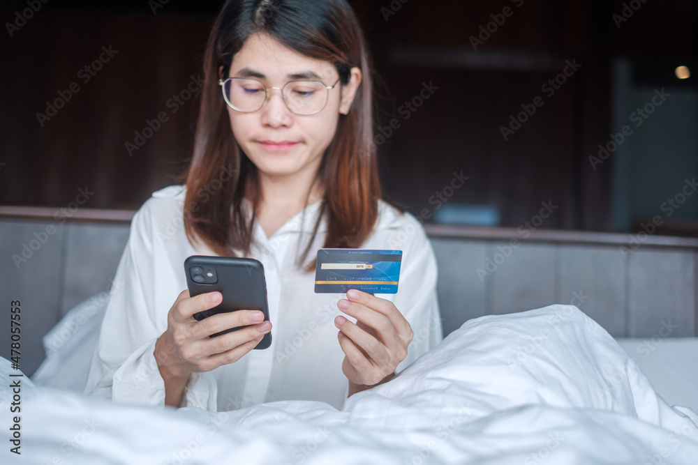 woman using mobile smart phone and credit card for online shopping while making order on bed in morning at home. technology, ecommerce, digital banking online payment and apartment living concept woman using mobile smart phone and credit card for online shopping while making order on bed in morning at home. technology, ecommerce, digital banking online payment and apartment living concept