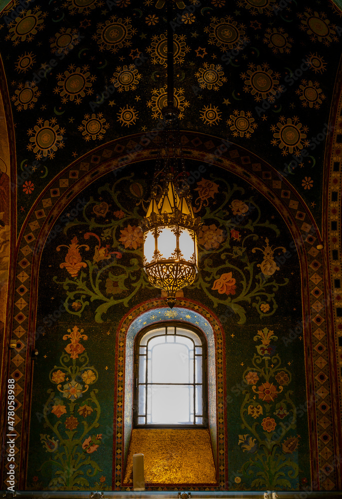 Antique chandelier and window on the background of a mosaic-covered wall in the Church of the Savior on Spilled Blood in St. Petersburg, Russia
