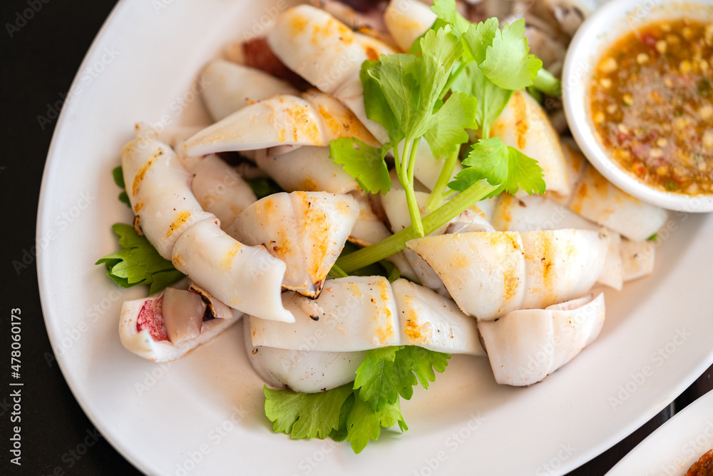 Grilled fresh squid, Close up Thai food Grilled fresh squid in white plate with spicy and sour sauce or seafood sauce, top view image. Grilled fresh squid, Close up Thai food Grilled fresh squid in white plate with spicy and sour sauce or seafood sauce, top view image.