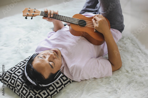Young asian man relaxing, lying down playing the ukelele while singing alone at home