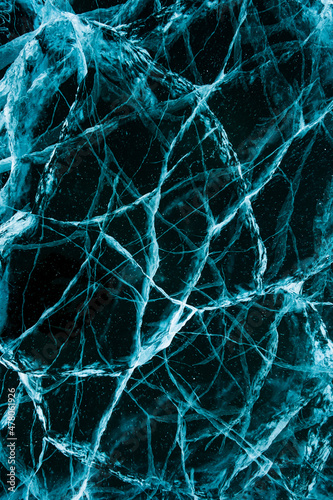 Texture of beautiful blue ice with cracks and air bubbles in the frozen lake. Winter nature background. Vertical photo.
