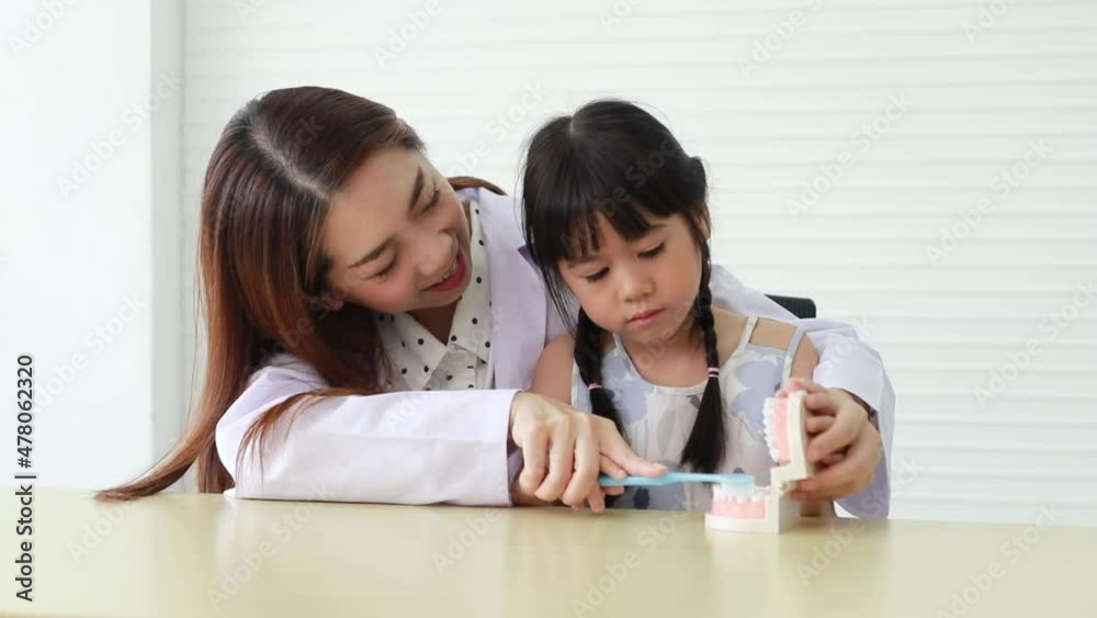 Female dentist teaches a little girl how to brush properly and is interested in a dental mockup of how to properly clean teeth and prevent cavities in the hospital office. Female dentist teaches a little girl how to brush properly and is interested in a dental mockup of how to properly clean teeth and prevent cavities in the hospital office.