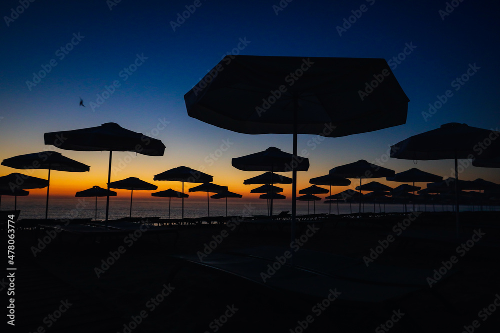 Silhouettes of sun umbrellas on the beach just before the sunrise on a calm and warm summer morning at the Black Sea in the Obzor resort in Bulgaria.