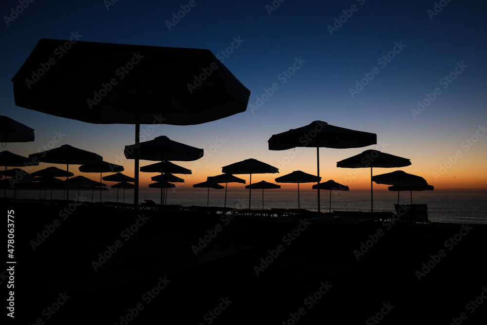 Silhouettes of sun umbrellas on the beach just before the sunrise on a calm and warm summer morning at the Black Sea in the Obzor resort in Bulgaria.