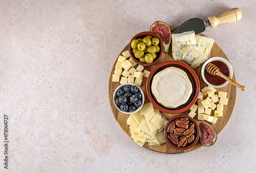 Top view of a tasty cheese board with berries, honey, nuts, olives, and cheese varieties on a circle kitchen plate. Party snack food, copy space.