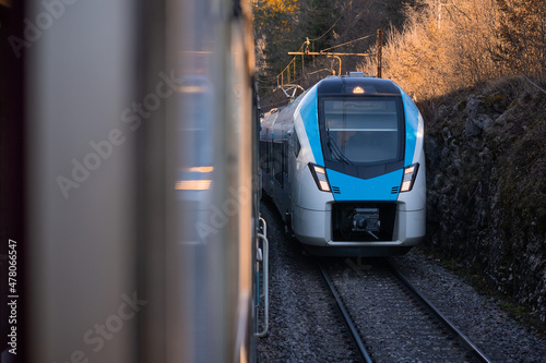  Modern blue and white passenger train coming towards another train on adjacent track. Two trains meeting on a parallel tracks.