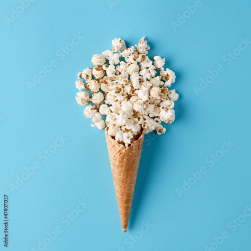Ice cream cone with spilled popcorn on pastel blue background.