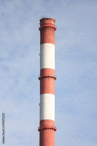 Tall, thin Two Color red and white chimney on the background of blue sky with clouds.