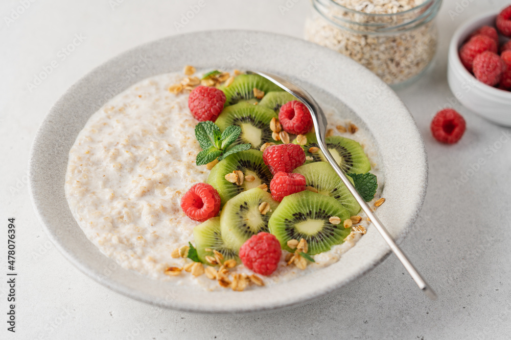 Oatmeal with kiwi and raspberries in ceramic bowl on light background with copy space. Healthy breakfast side view Oatmeal with kiwi and raspberries in ceramic bowl on light background with copy space. Healthy breakfast side view