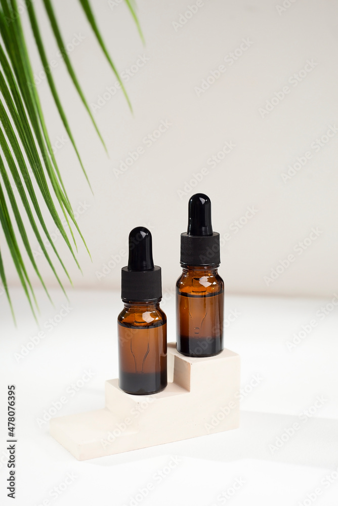 Amber glass bottles with dropper pipette with serum or essential oil on concrete plate for product presentation with palm leaves. Skin care cosmetic. Beauty concept for face body care Amber glass bottles with dropper pipette with serum or essential oil on concrete plate for product presentation with palm leaves. Skin care cosmetic. Beauty concept for face body care