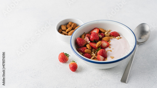 Strawberry yogurt with fresh berries, homemade granola, almonds in bowl. Healthy breakfast on light background