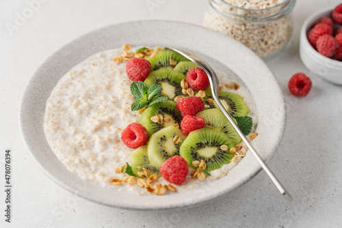 Oatmeal with kiwi and raspberries in ceramic bowl on light background with copy space. Healthy breakfast side view
