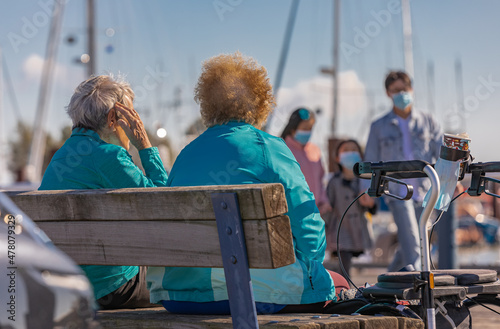 Two senior women or friends drinking coffee and talking outdoor.Two elderly women sit on bench near pier at autumn