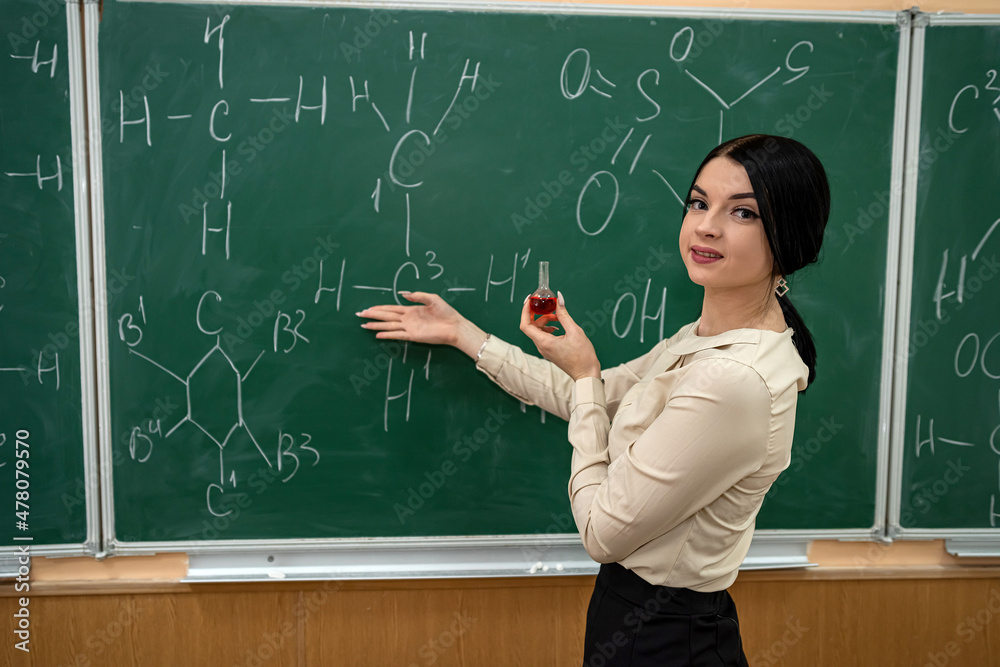 young pretty teacher learn lesson on chemistry and standing near blackboard with chemical formula young pretty teacher learn lesson on chemistry and standing near blackboard with chemical formula