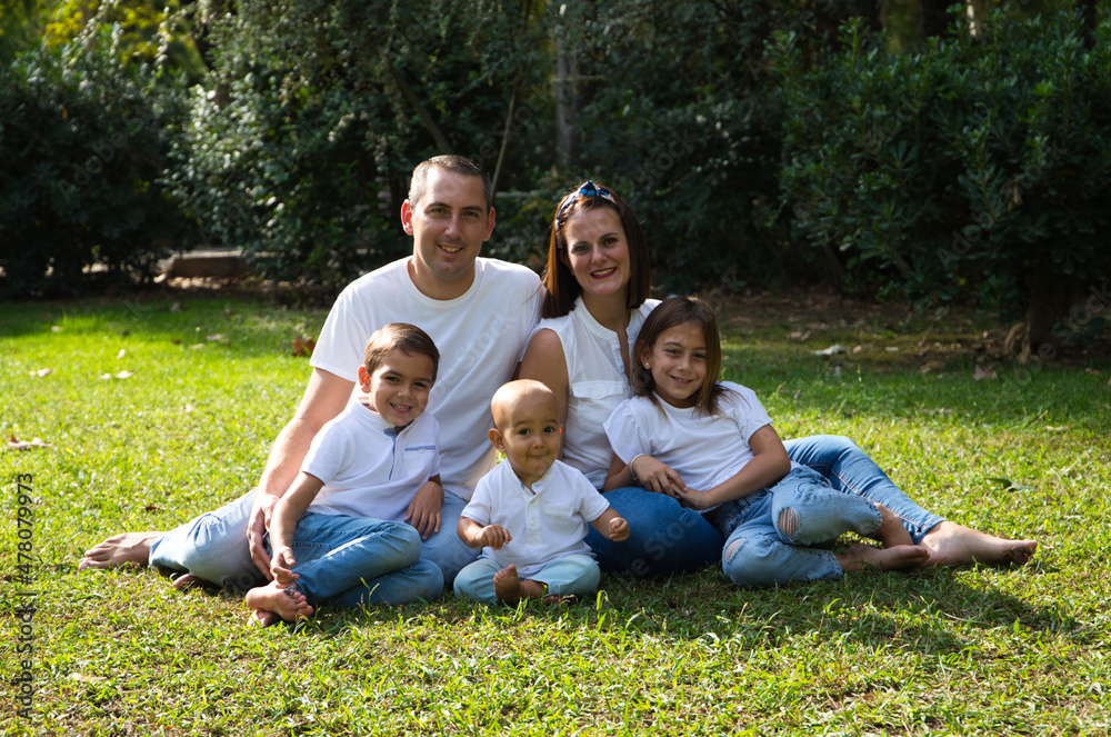 Portrait of happy parents with their three children lying in the park. The eldest daughter is a transgender girl. Concept of family happy united family with children.