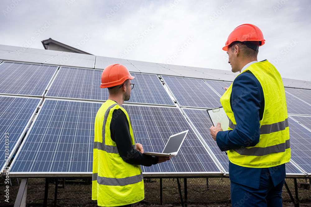 young worker in overalls with boss in overalls looking at newly installed solar panels. young worker in overalls with boss in overalls looking at newly installed solar panels.