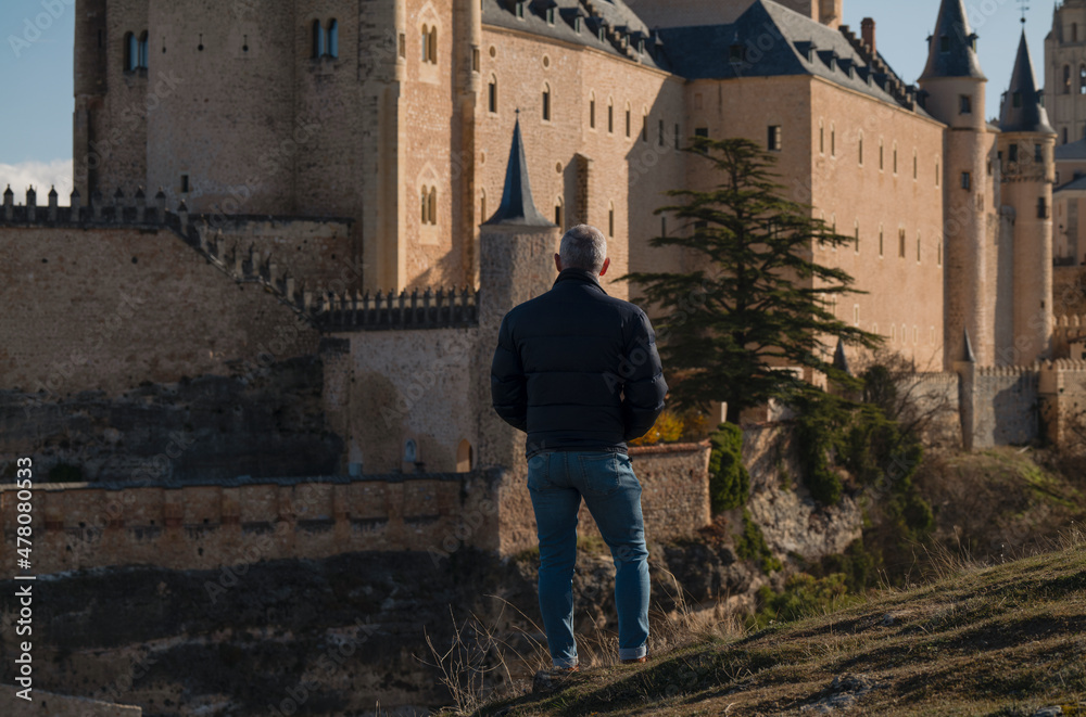 Rear view of adult man standing on hill looking at view of Castle of Segovia, Spain