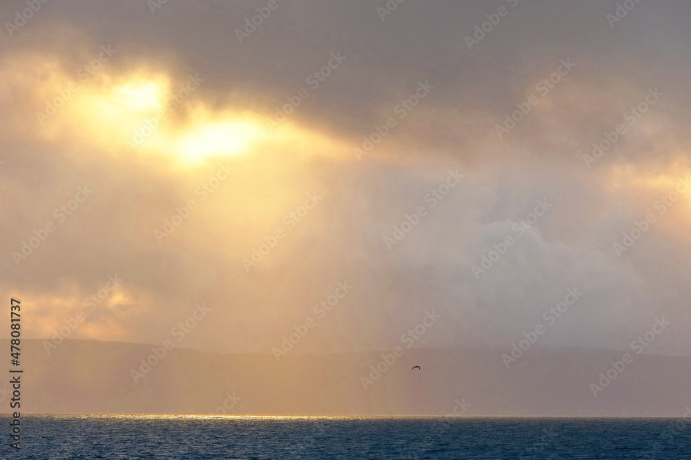 Dramatic cloudy sky with sun beam over calm ocean surface. Peaceful and calm atmosphere