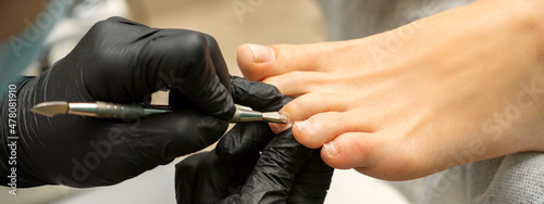Cuticle Removal on Toes. Hands in black gloves of pedicure master remove cuticle on female toes by pusher photo