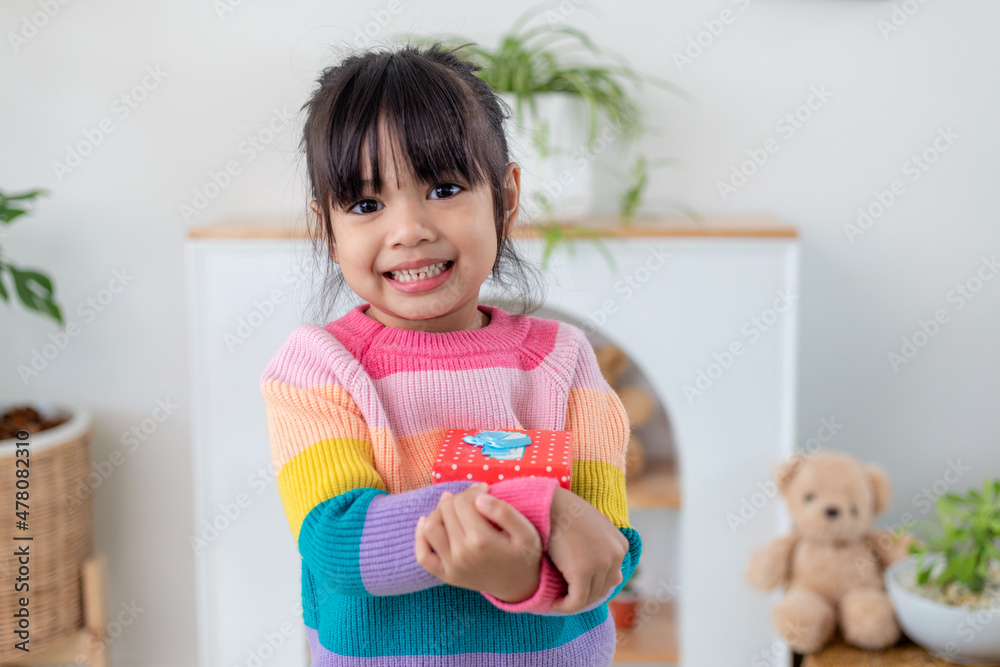 Little Asian girl smile and excited and holding red gift box in living room background. child holding gift box in Christmas and New year.Asian child girl smile and surprise. Little Asian girl smile and excited and holding red gift box in living room background. child holding gift box in Christmas and New year.Asian child girl smile and surprise.