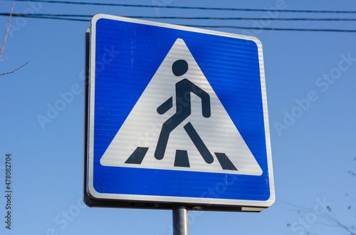 A road sign for a crosswalk. Blue sign against the blue sky. Day