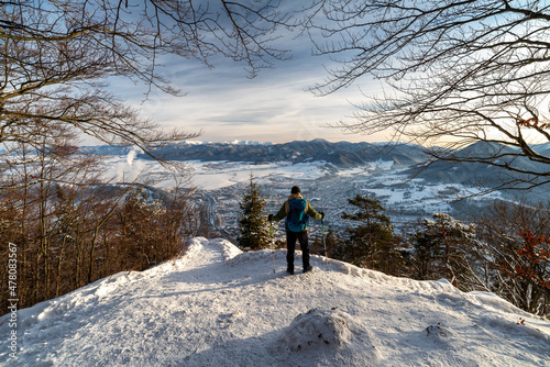 Hiker wih trekking poles and backpack looking from top of the hill on winter snowy landscape. Hill Cebrat over town Ruzomberok, Slovakia photo