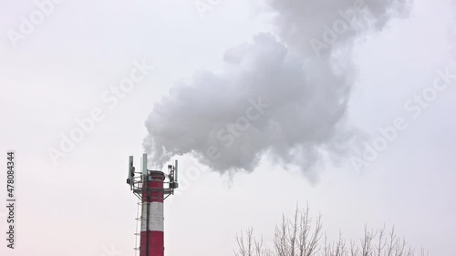 Thermal power station pipe at winter with outgoing smoke, steam and isicles on telecommunication antennas photo