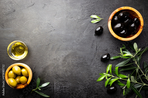 Black olives and olive oil in wooden bowls on black background. Top view with copy space for text.