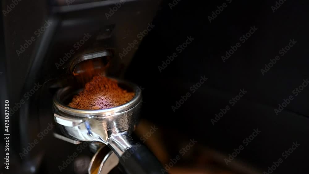 Portafilter with ground coffee near grinder