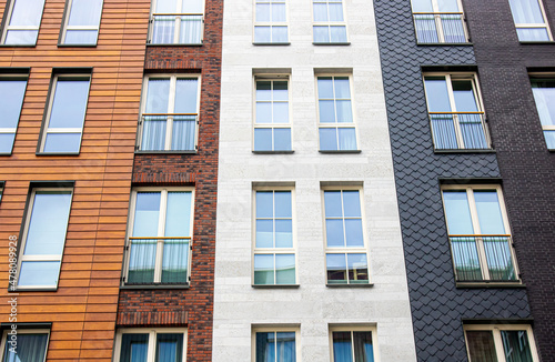 Modern apartment building exterior facade with lot of different materials: wood, stone bricks. Lot of white frame windows.