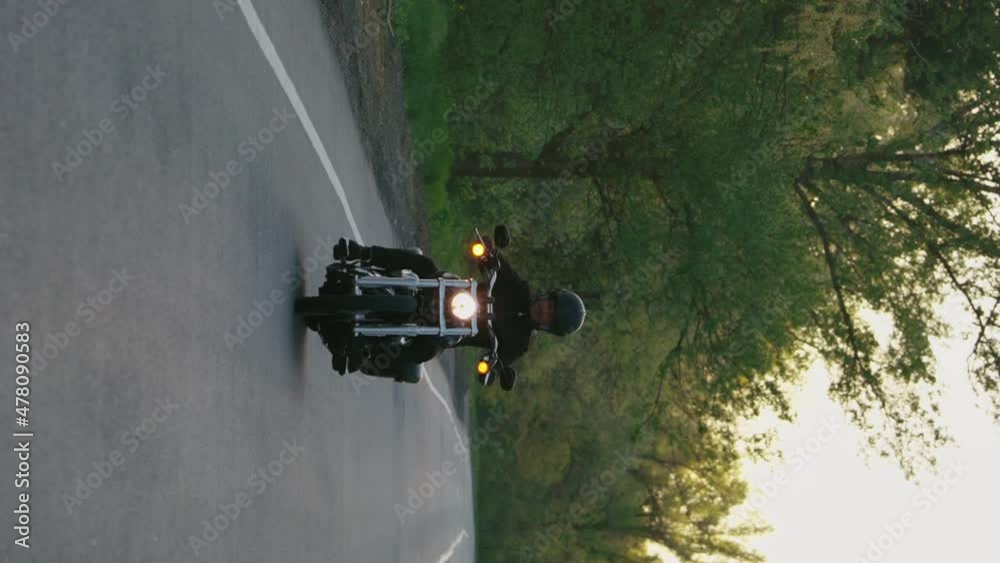 Vertical Screen: Man in black clothes and helmet riding motorcycle at sunset in slow motion, signs on roadsides. Tracking shot biker on his ride. Safety and traffic rules. Concept of transport Vertical Screen: Man in black clothes and helmet riding motorcycle at sunset in slow motion, signs on roadsides. Tracking shot biker on his ride. Safety and traffic rules. Concept of transport