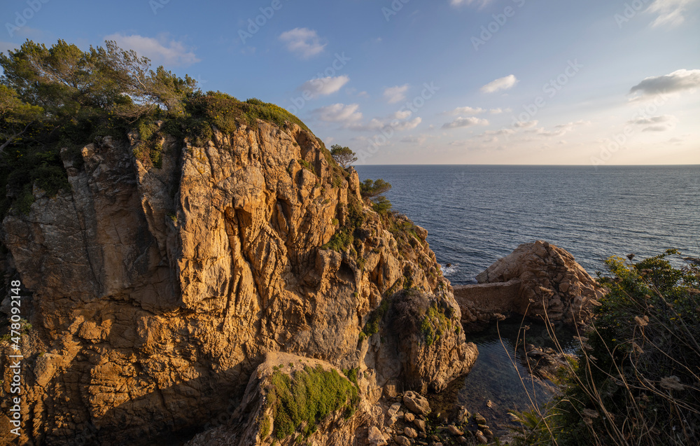 Seascape. Mediterranean evening. Rocks surrounded by water on the beach protruding into the sea on a sunny day, Blanes, Catalonia, Spain. Seascape. Mediterranean evening. Rocks surrounded by water on the beach protruding into the sea on a sunny day, Blanes, Catalonia, Spain.