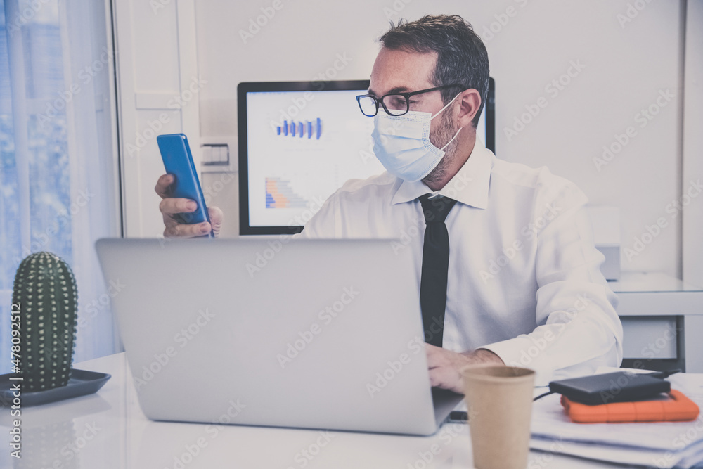 Business man with surgical masks working in the office during lockdown for coronavirus covid-19. Male sitting at the desk works with laptop at home. Health care, quarantine, remote working concept. Business man with surgical masks working in the office during lockdown for coronavirus covid-19. Male sitting at the desk works with laptop at home. Health care, quarantine, remote working concept.