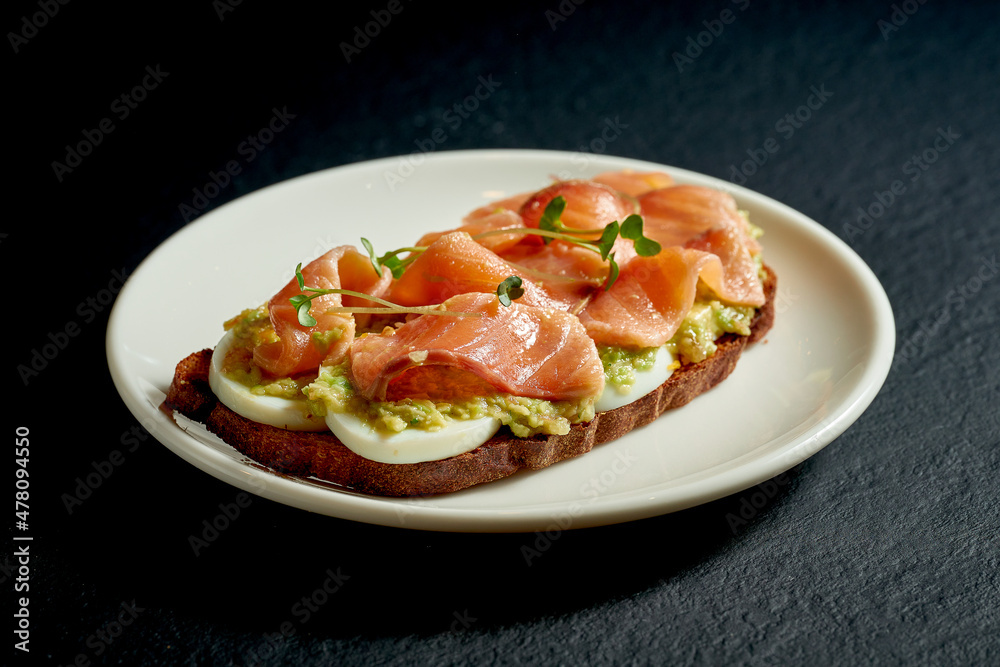 Toast with salmon and avocado mousse in a white plate on a black background Toast with salmon and avocado mousse in a white plate on a black background