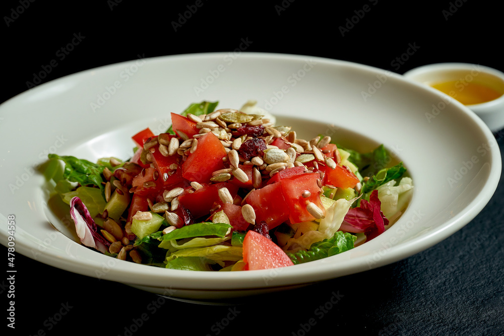 Diet salad with tomatoes and cucumbers, seeds in a white plate on a black background Diet salad with tomatoes and cucumbers, seeds in a white plate on a black background